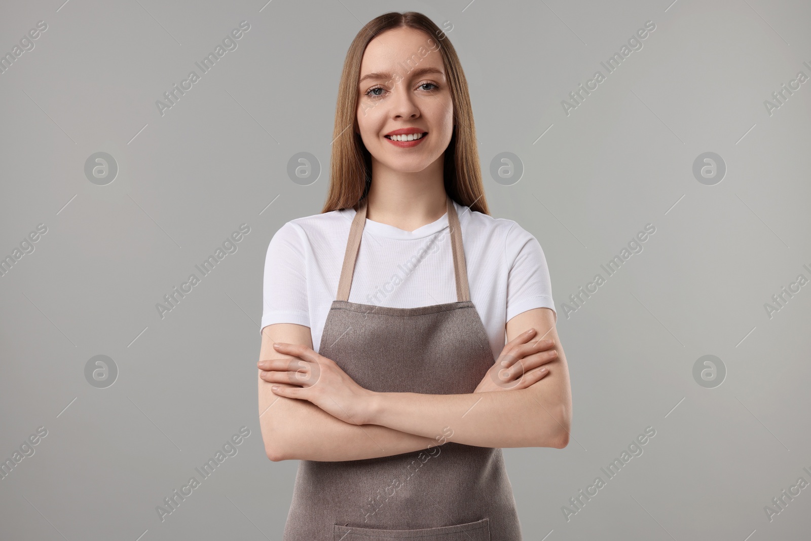 Photo of Beautiful young woman wearing kitchen apron on grey background. Mockup for design