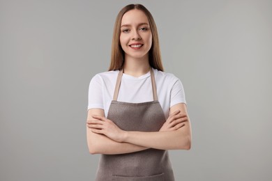 Beautiful young woman wearing kitchen apron on grey background. Mockup for design