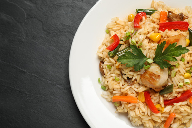 Photo of Delicious rice pilaf with chicken and vegetables on black table, closeup. Space for text