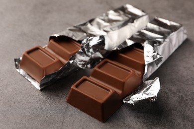 Photo of Tasty chocolate bars wrapped in foil on grey table, closeup