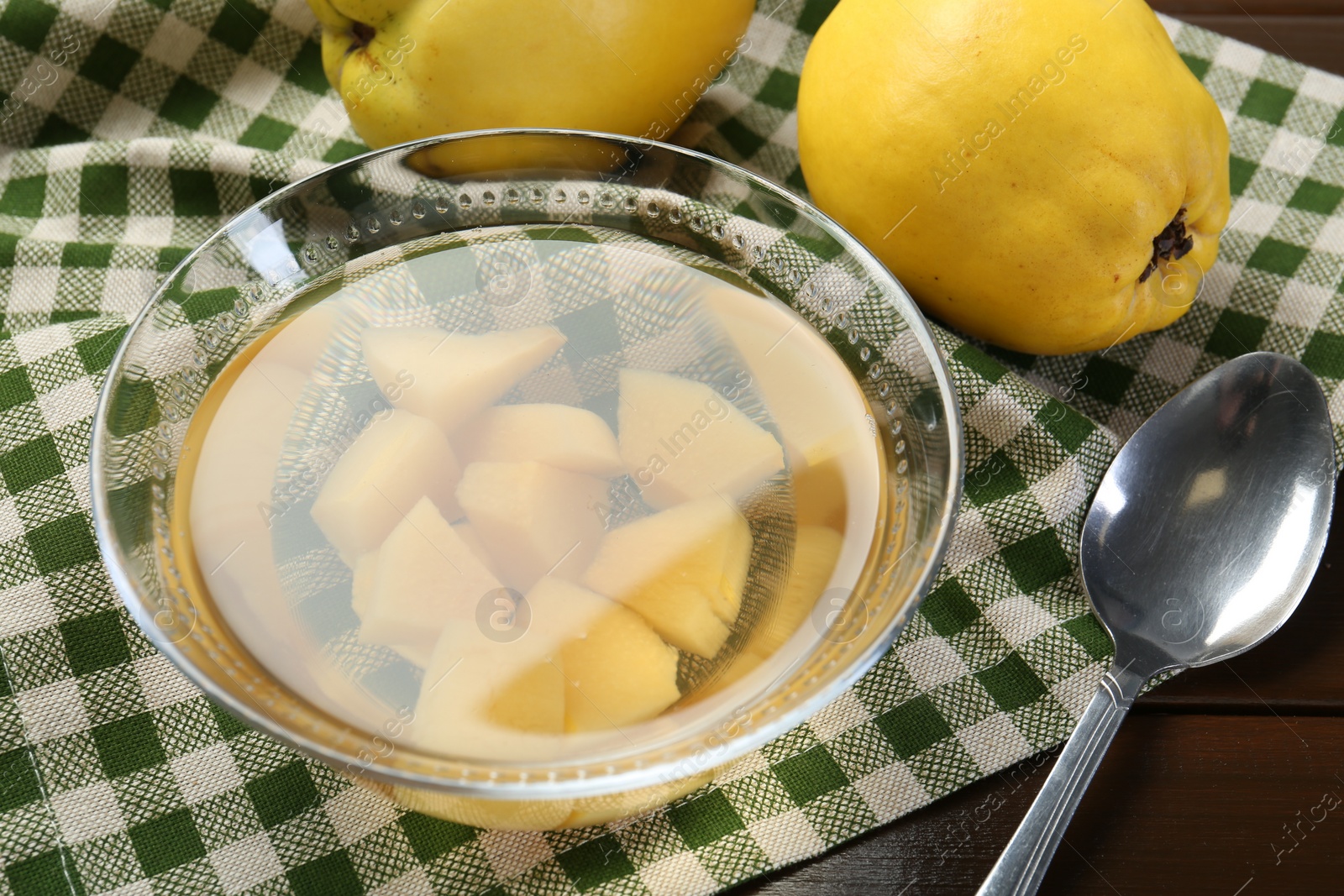 Photo of Delicious quince drink in glass bowl, fresh fruits and spoon on wooden table, closeup
