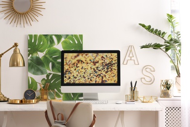 Photo of Modern workplace with computer and golden decor on desk near wall. Stylish interior design