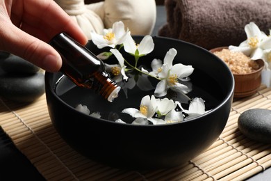 Photo of Woman dripping jasmine essential oil into bowl on table, closeup