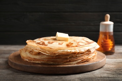 Wooden board with thin pancakes and butter on table