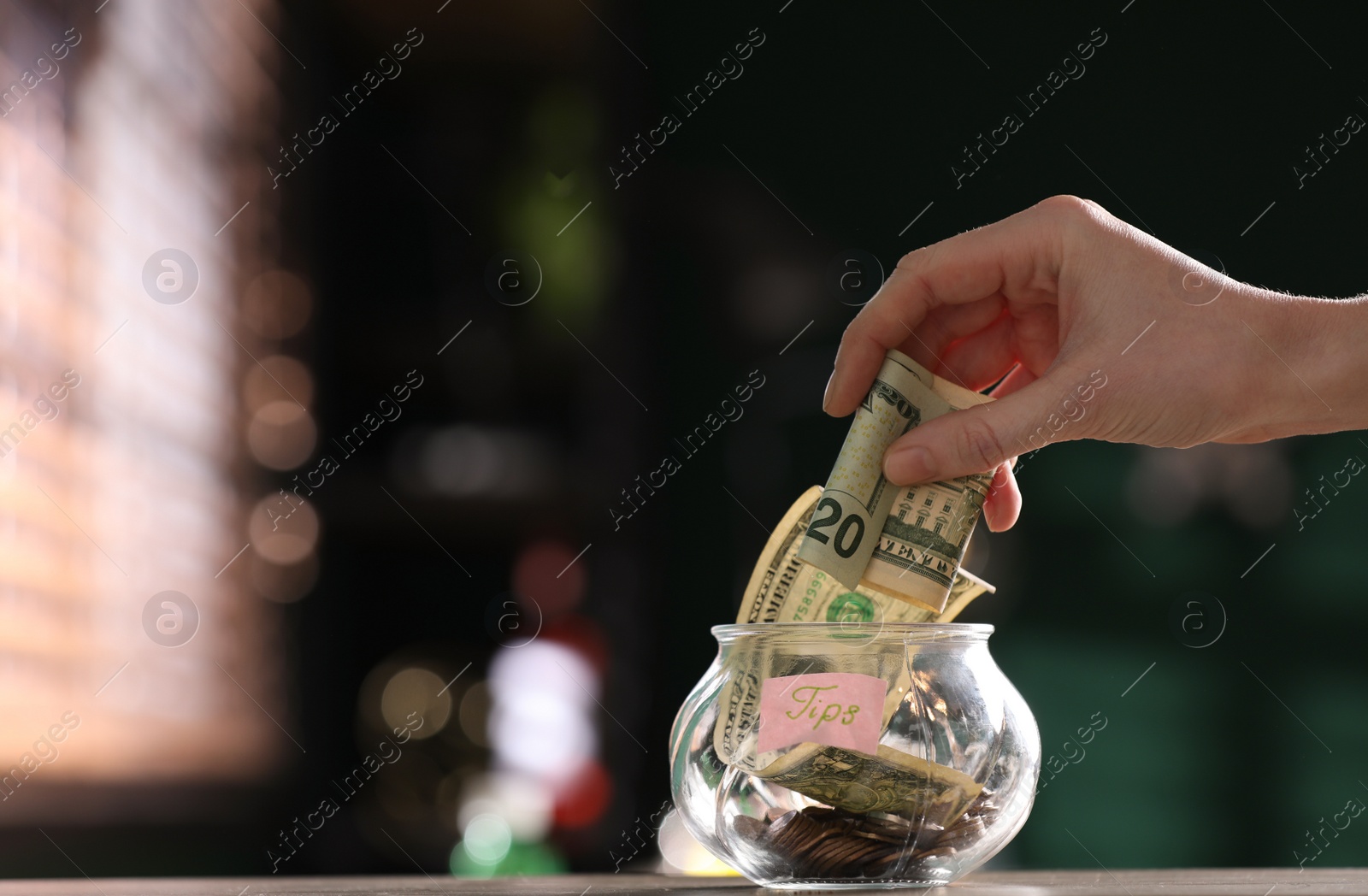 Photo of Woman putting tips into glass vase on wooden table indoors, closeup. Space for text