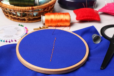 Blue cloth with stitches, sewing thread, needle and scissors on light table, closeup