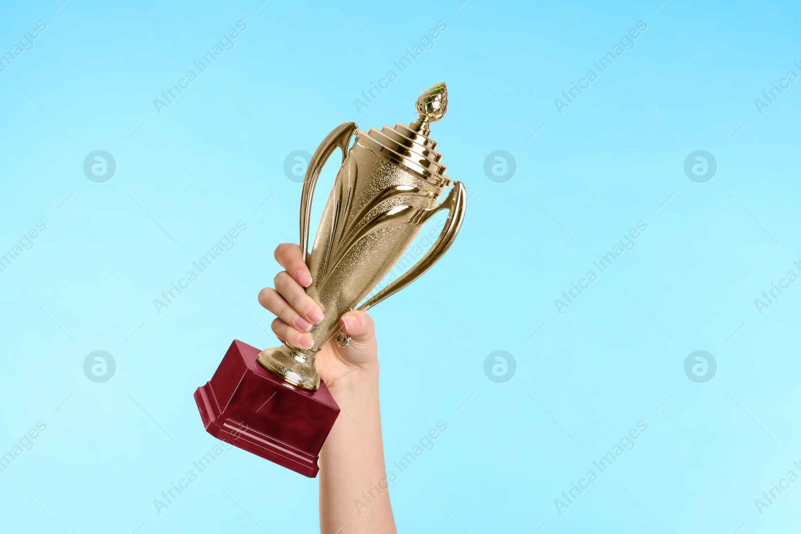 Photo of Woman holding gold trophy cup on light blue background, closeup