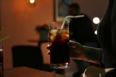 Photo of Woman with glass of cold cola in dark cafe, closeup. Space for text