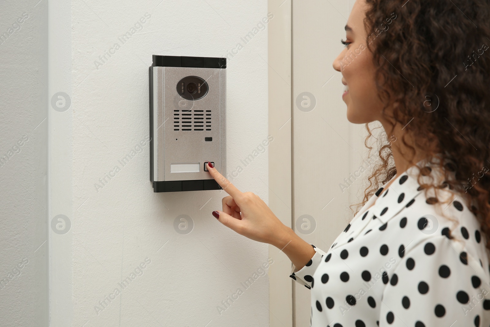 Photo of Young African-American woman ringing intercom with camera in entryway