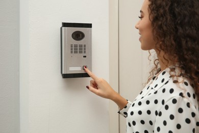 Photo of Young African-American woman ringing intercom with camera in entryway