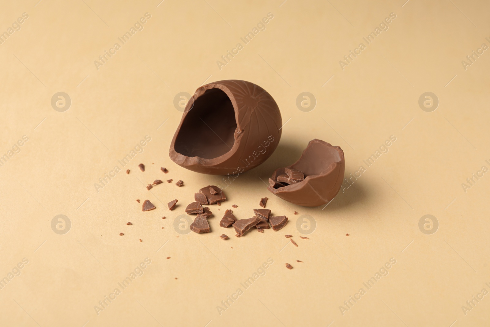 Photo of Broken milk chocolate egg on beige background