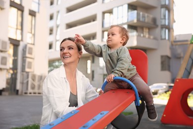 Photo of Happy nanny and cute little boy on seesaw outdoors