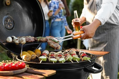 Man with drink cooking meat and vegetables on barbecue grill outdoors, closeup