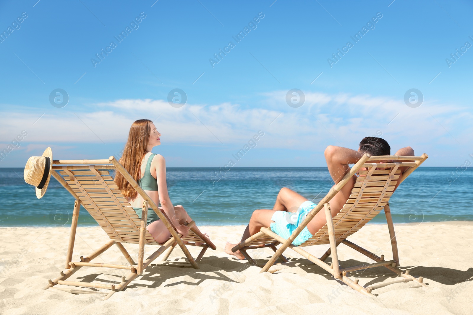 Photo of Woman in bikini and her boyfriend on deck chairs at beach. Lovely couple