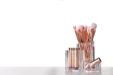 Photo of Organizer with different makeup brushes and lipsticks on white table