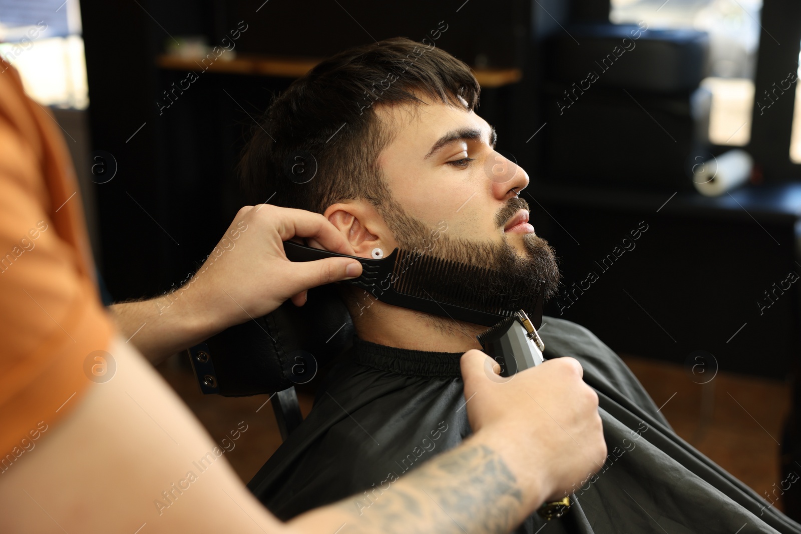 Photo of Professional hairdresser working with bearded client in barbershop