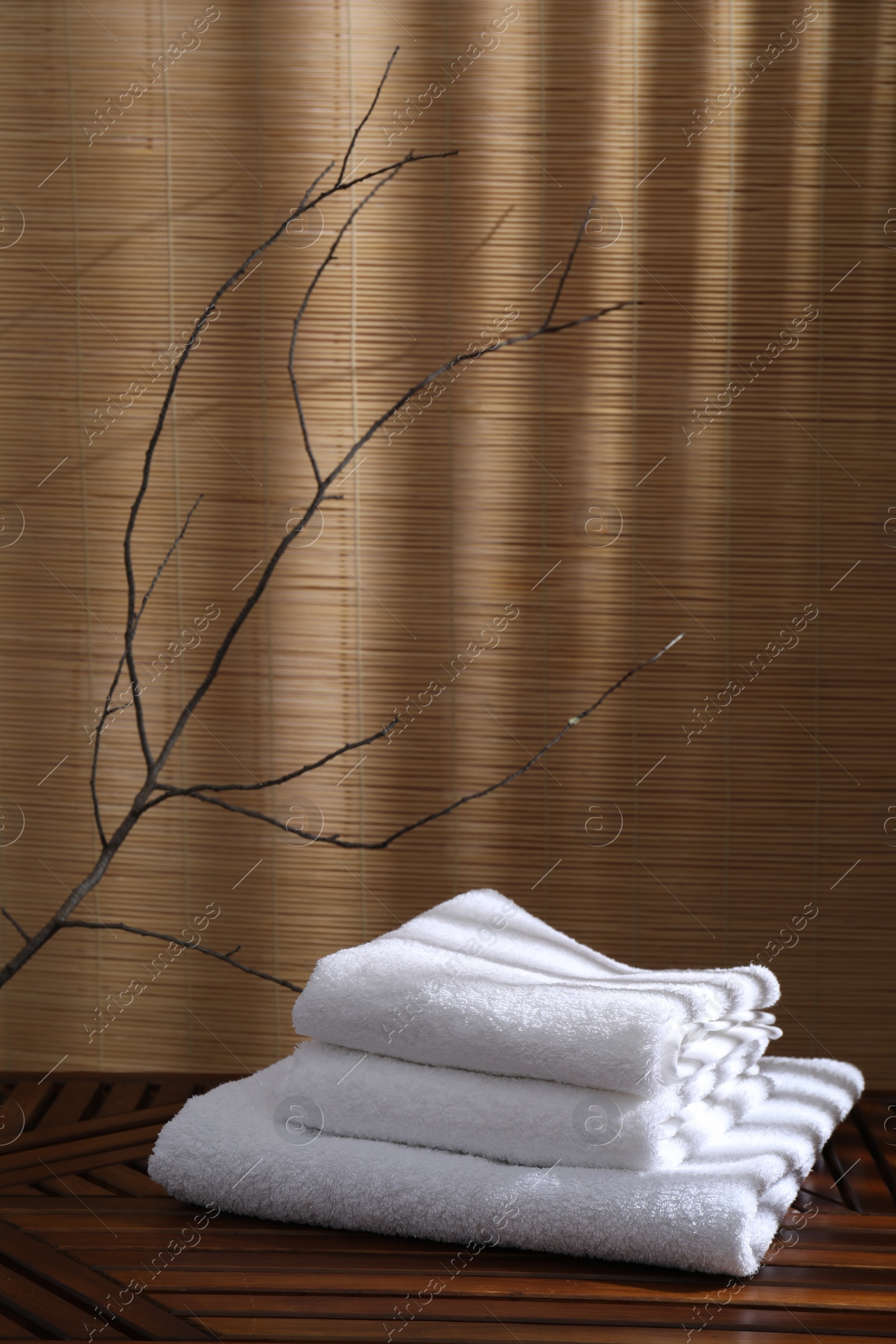 Photo of Stacked soft towels on wooden table and tree branches indoors