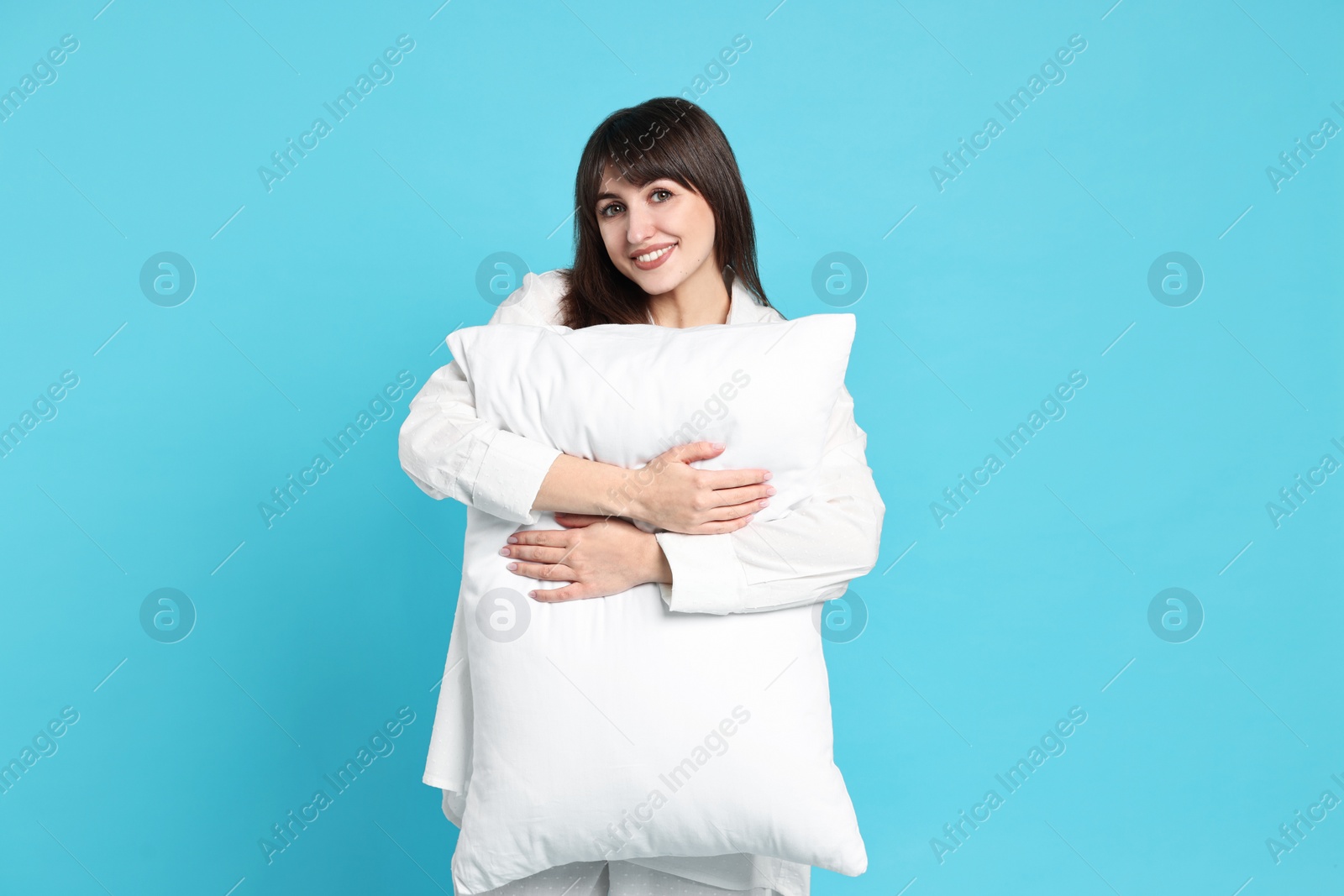 Photo of Happy woman in pyjama holding pillow on light blue background