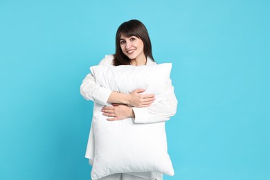 Happy woman in pyjama holding pillow on light blue background