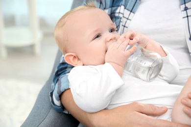 Photo of Lovely mother giving her baby drink from bottle in room, closeup