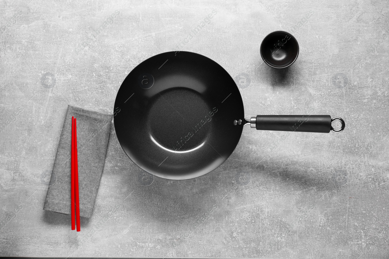 Photo of Empty iron wok, sauce bowl and chopsticks on grey table, flat lay