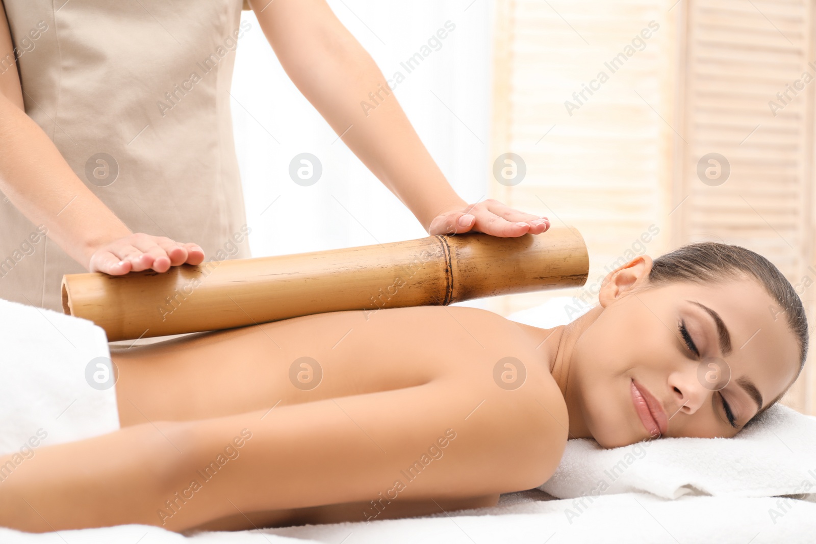 Photo of Young woman having massage with bamboo stick in wellness center