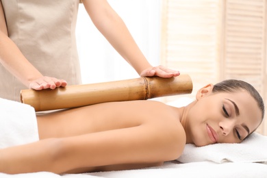 Photo of Young woman having massage with bamboo stick in wellness center