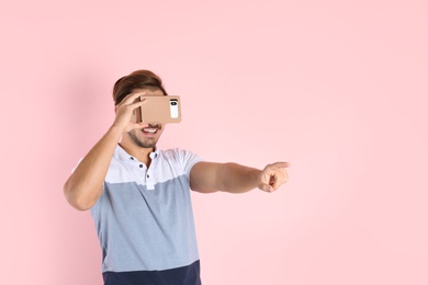 Photo of Young man using cardboard virtual reality headset on color background. Space for text