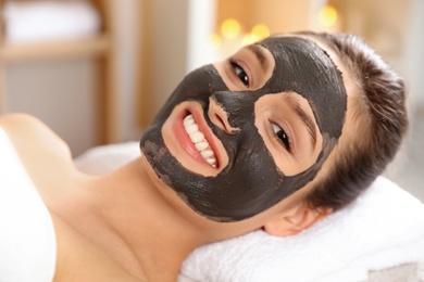 Beautiful woman with black mask on face relaxing in spa salon