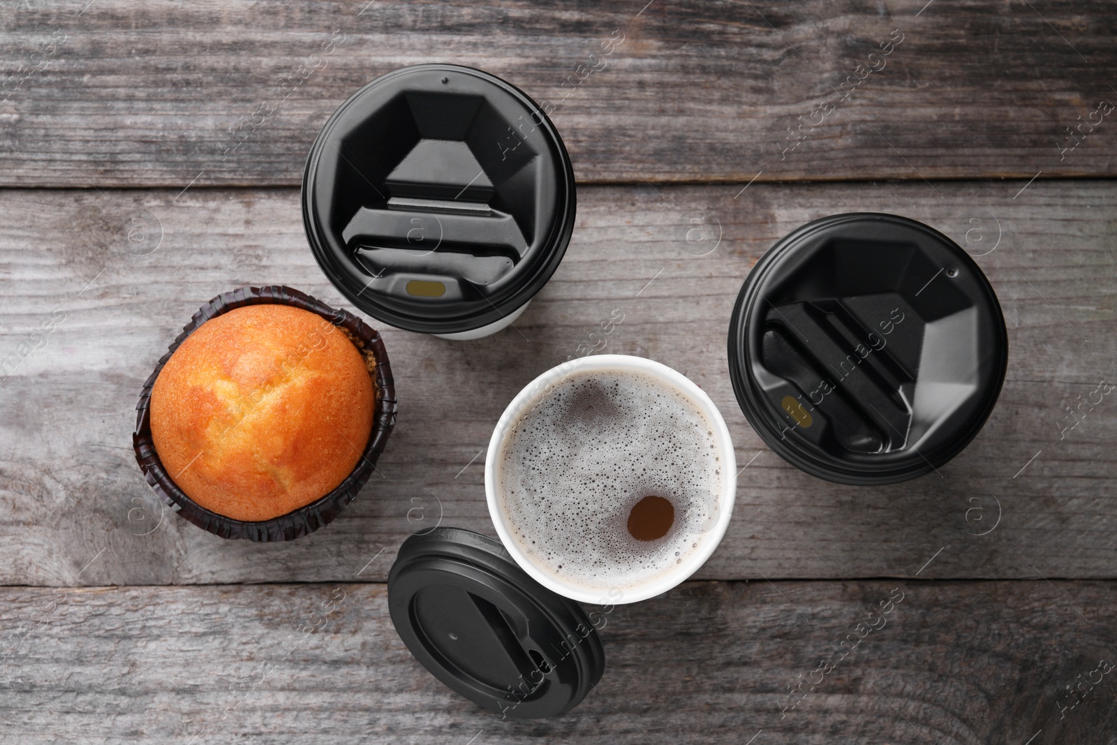 Photo of Coffee to go. Paper cups with tasty drink and muffin on wooden table, flat lay
