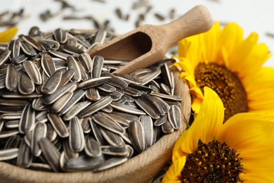 Photo of Raw sunflower seeds in bowl and flowers, closeup