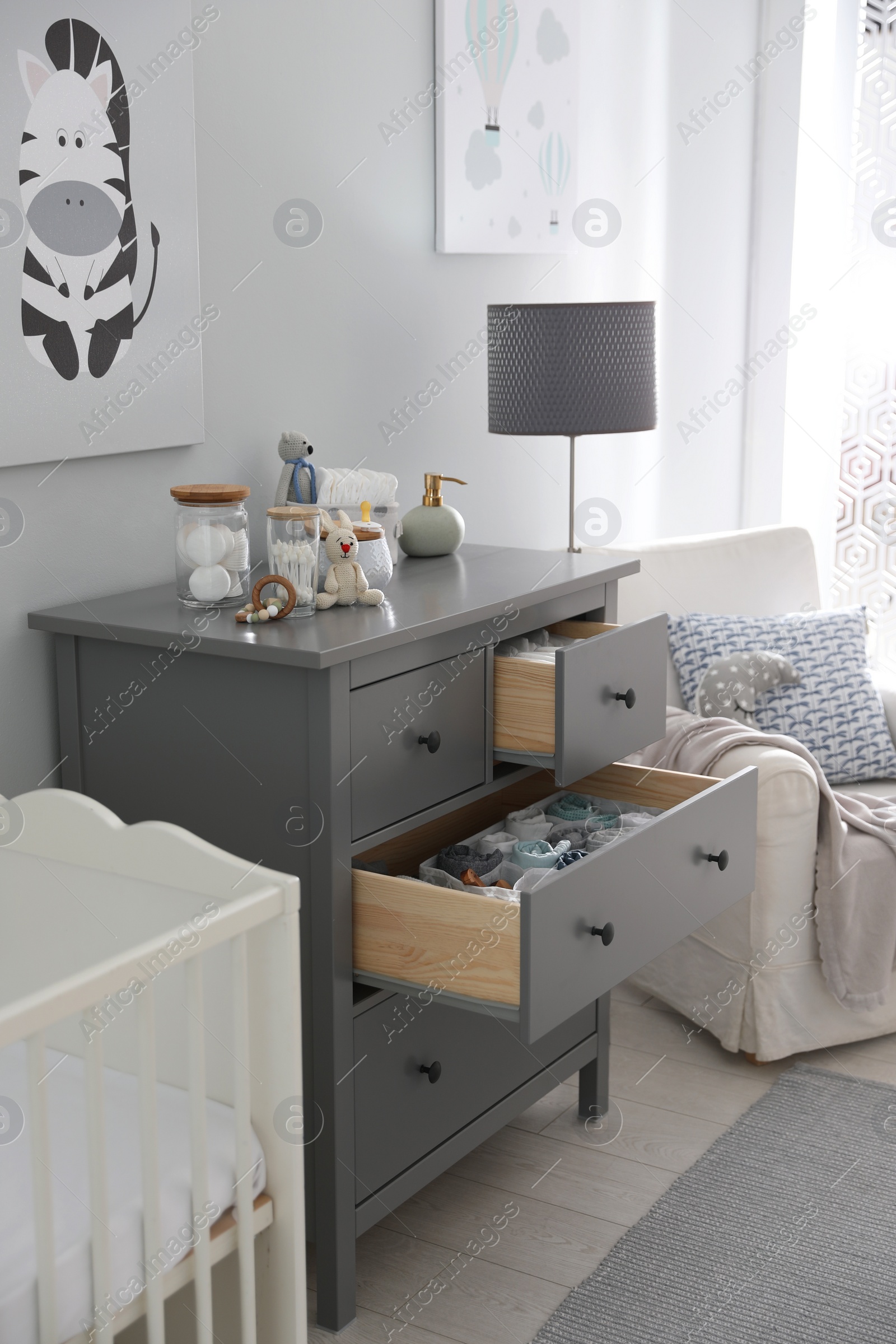 Photo of Modern open chest of drawers with baby clothes and accessories in room