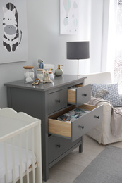 Photo of Modern open chest of drawers with baby clothes and accessories in room