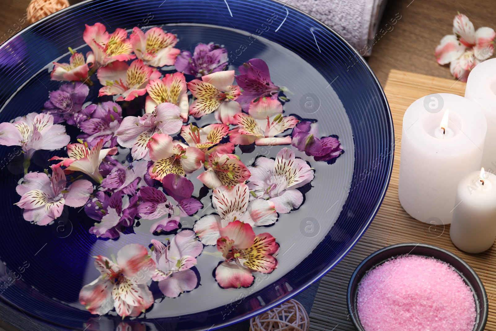 Photo of Bowl of water with flowers, sea salt and candles on table. Spa treatment