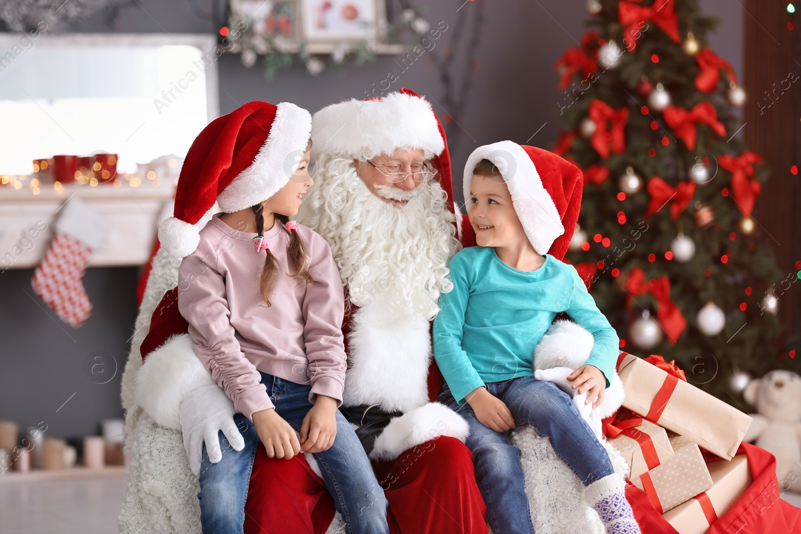 Photo of Little children sitting on authentic Santa Claus' knees indoors