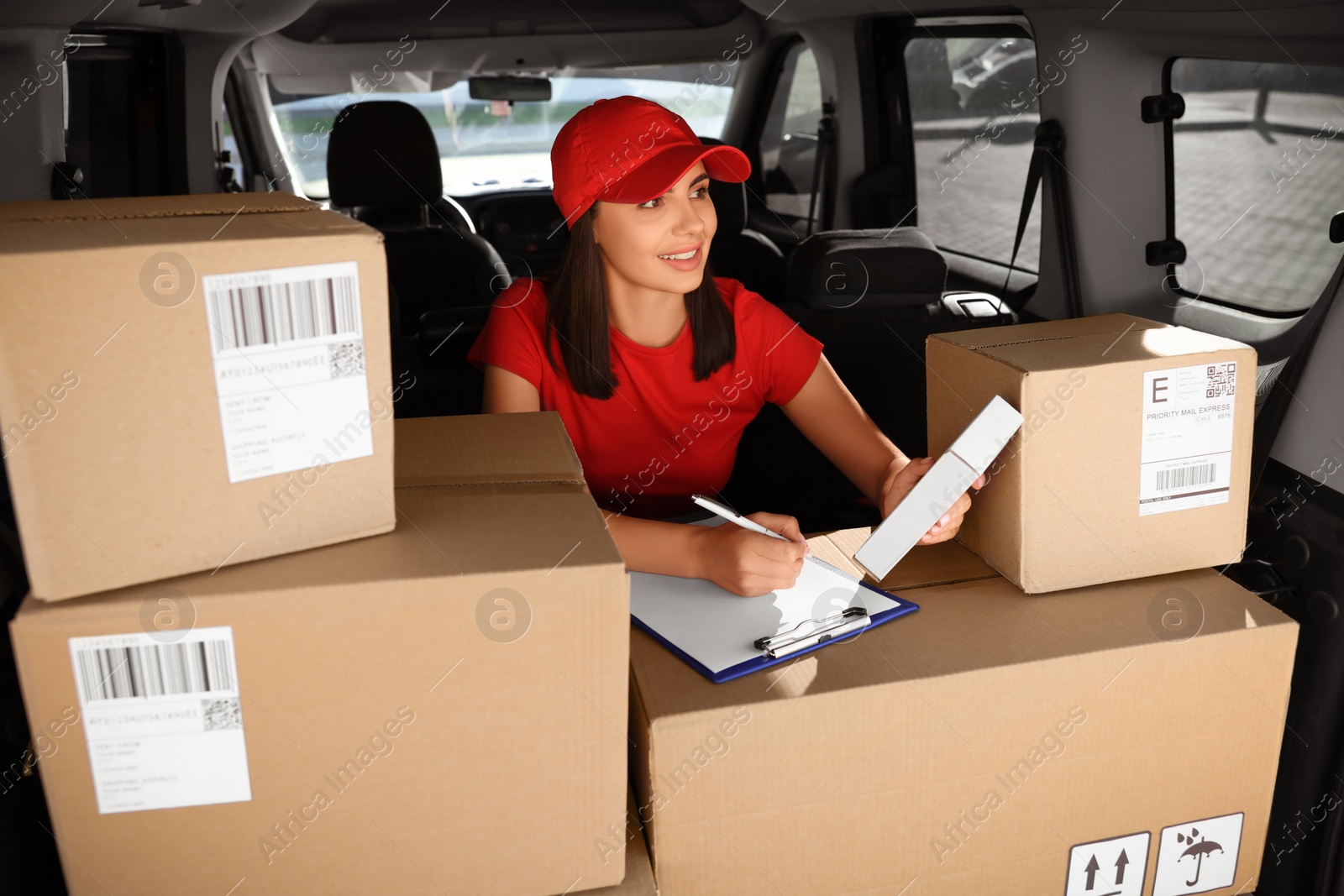 Photo of Courier with clipboard checking packages in delivery van