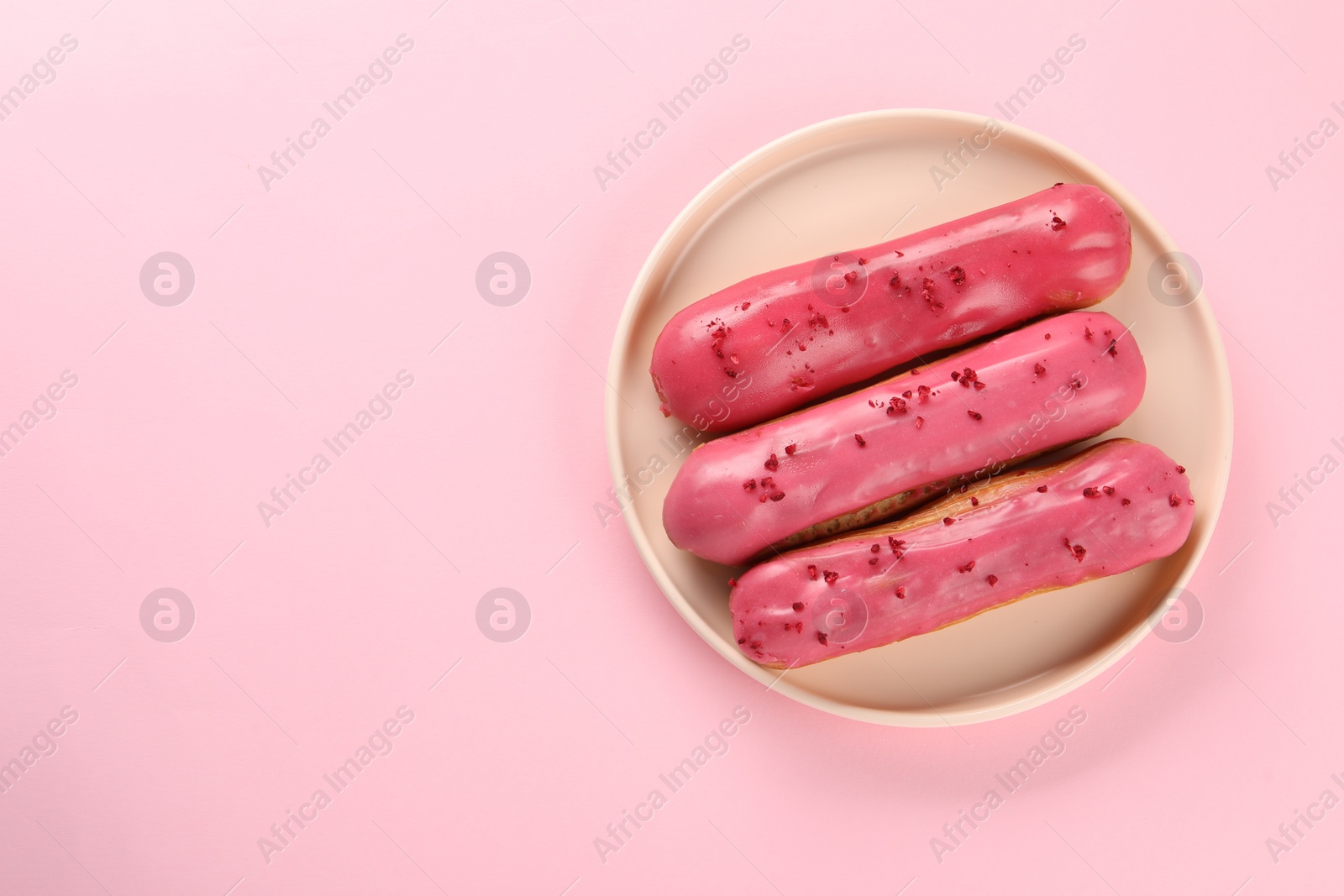 Photo of Delicious eclairs covered with glaze on pink background, top view. Space for text