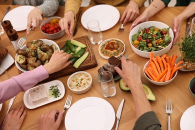 Photo of Friends eating vegetarian food at wooden table indoors, closeup
