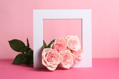 Photo of White frame and beautiful roses on pink table