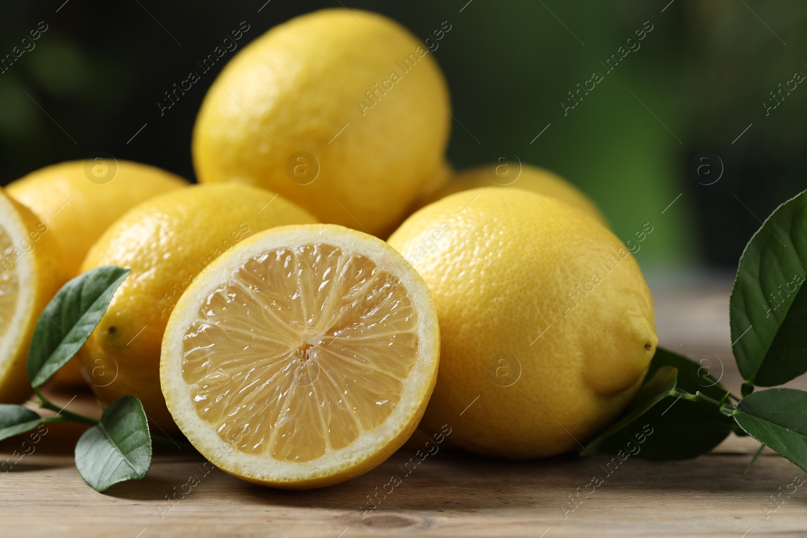 Photo of Fresh lemons and green leaves on wooden table, closeup