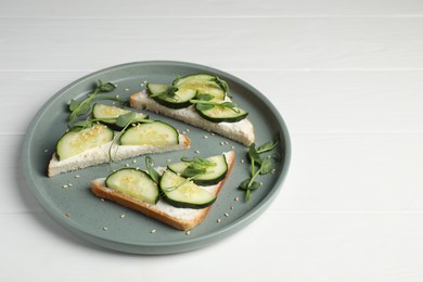 Photo of Tasty cucumber sandwiches with sesame seeds and pea microgreens on white wooden table