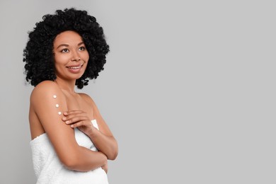 Photo of Young woman applying body cream onto arm on grey background. Space for text