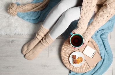 Woman and cup of hot winter drink on floor at home, top view