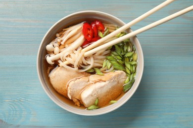 Photo of Delicious ramen with meat in bowl and chopsticks on light blue wooden table, top view. Noodle soup