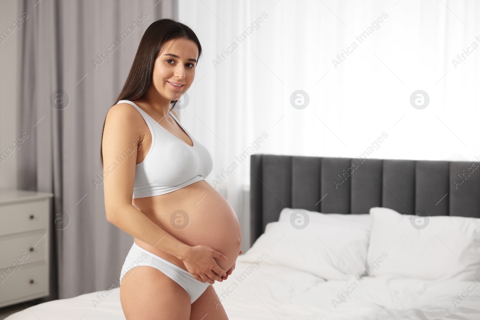 Photo of Beautiful pregnant woman wearing stylish comfortable underwear in bedroom, space for text