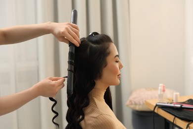 Photo of Hair styling. Hairdresser curling woman's hair in salon, closeup