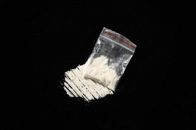 Photo of Drug addiction. Plastic bag with cocaine on black background, above view