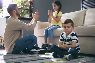 Unhappy little boy feeling jealous while father spending time with his sister at home