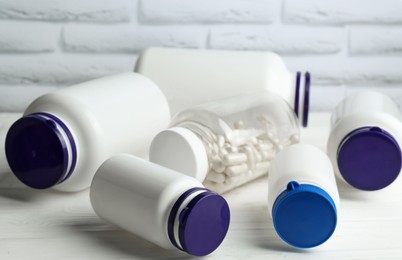 Medical bottles with pills on white wooden table, closeup