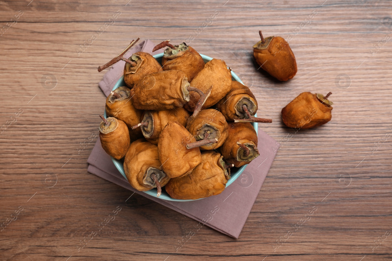 Photo of Bowl with tasty dried persimmon fruits on wooden table, flat lay